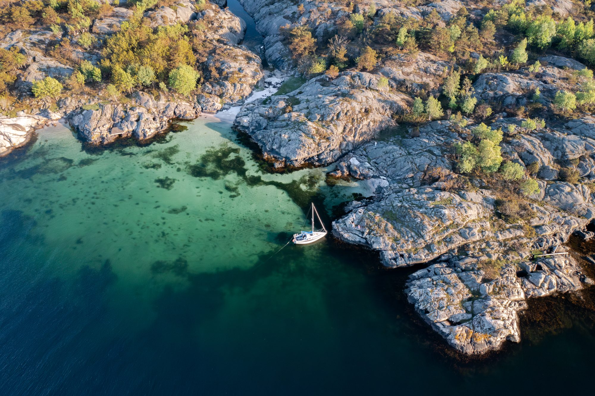 A sailboat anchored in a turquoise cove near Risør